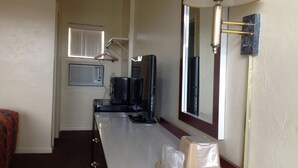 Habitación de hotel con cama, escritorio con lámpara, espejo, televisión y ventana.