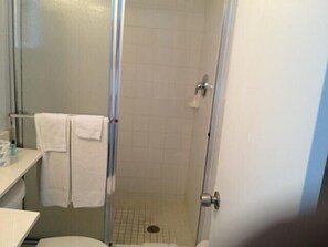 A bathroom with a glass shower enclosure, a toilet, and a sink with a towel hanging on the wall.