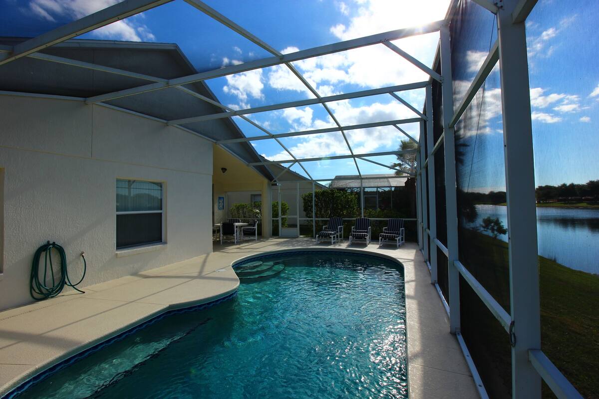 Una piscina interior con cerramiento de vidrio, un área de patio con sillas y vistas a un lago.