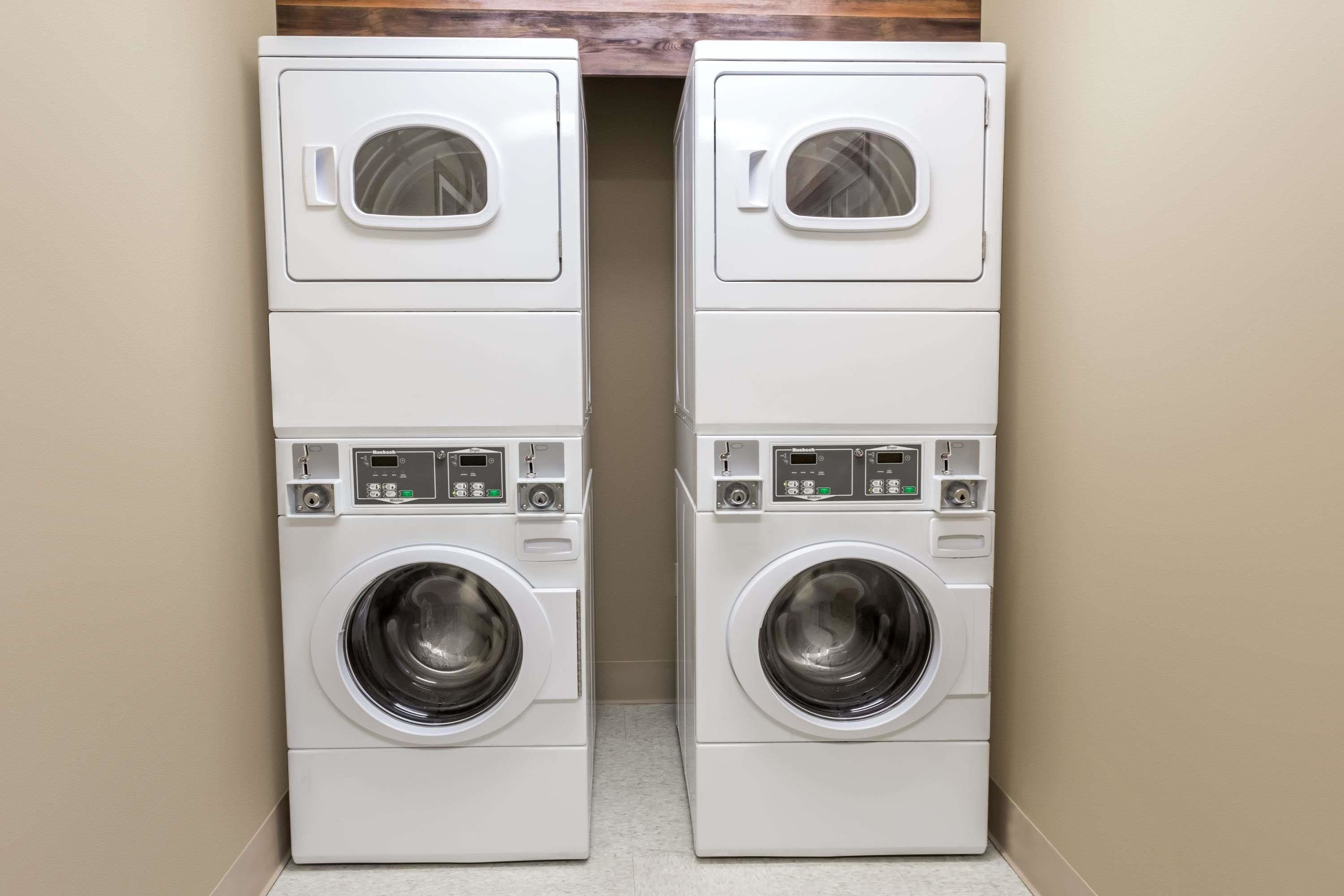Two stacked front-loading washers in a laundry room with a wooden shelf above.