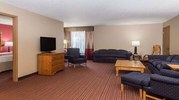 Habitación de hotel con una cama grande, un televisor, dos sofás, un aparador de madera y una pequeña mesa.