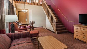 Una sala de estar con un sofá, una mesa de centro de madera, un televisor, una escalera y un comedor con sillas y una mesa.