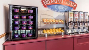 Una estación de desayuno con recipientes de yogur, manzanas, naranjas y dispensadores de cereales.