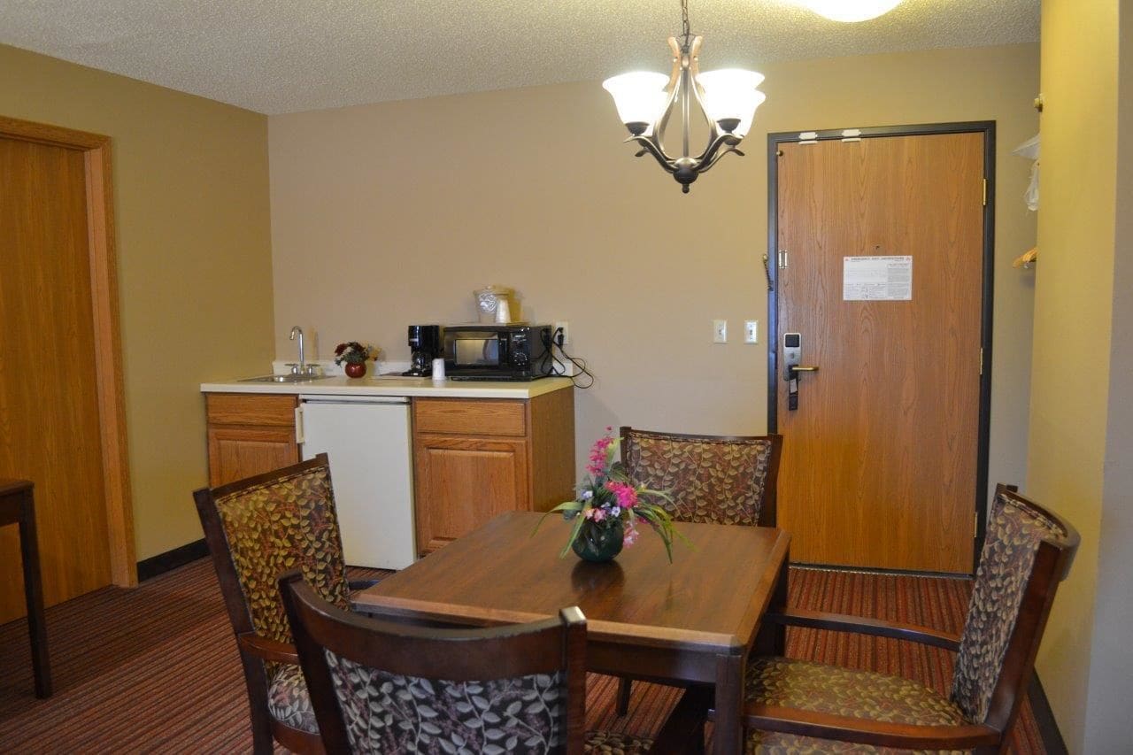 A dining area with a wooden table and chairs, a chandelier, a microwave, and a refrigerator.