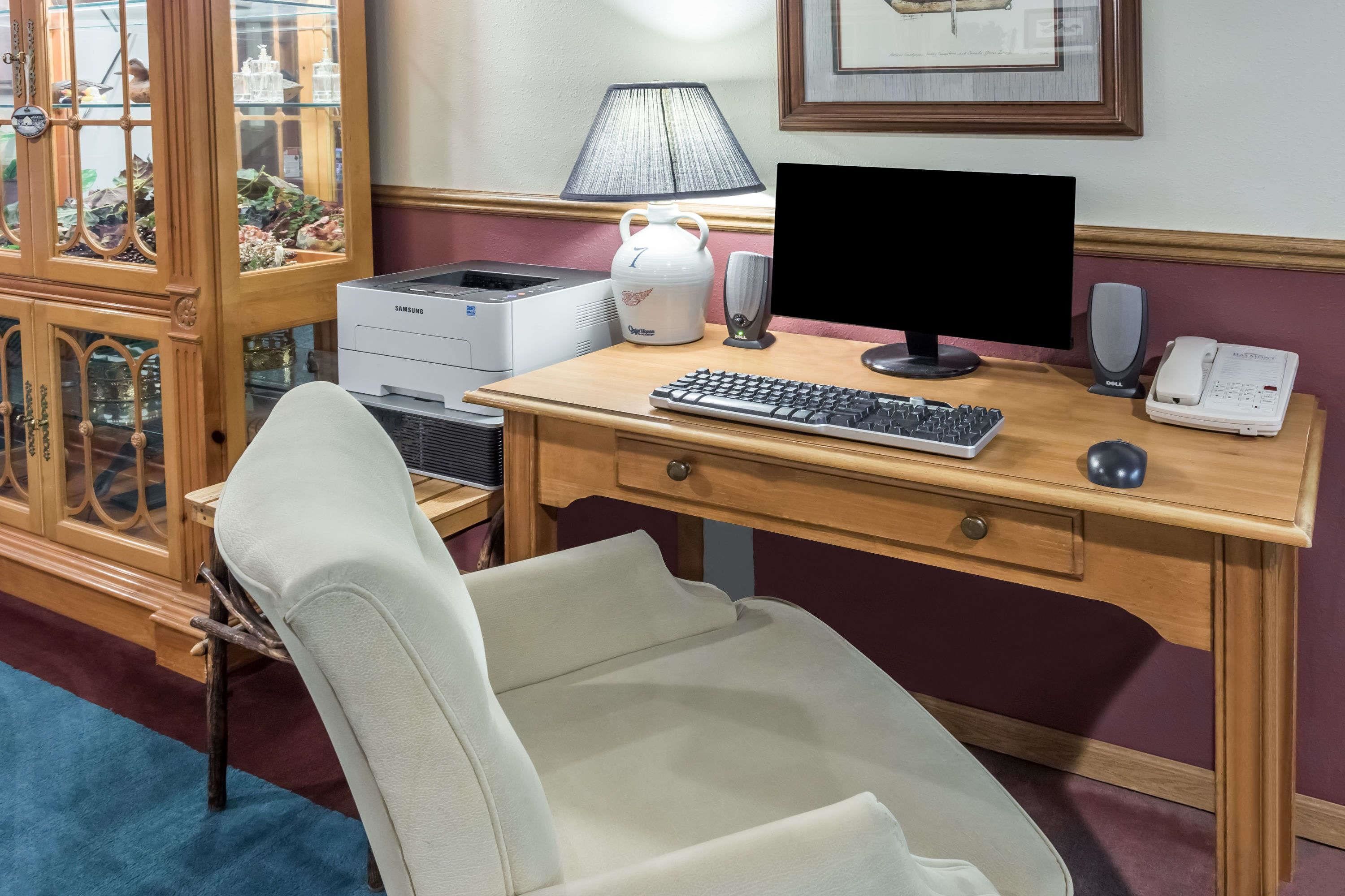 Un bureau en bois avec un ordinateur, un clavier et une souris, une lampe, un téléphone et un meuble décoratif doté de portes en verre.