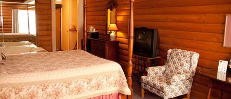 Un dormitorio de estilo cabaña de troncos con una cama con dosel, un aparador de madera, un sillón estampado y un televisor.