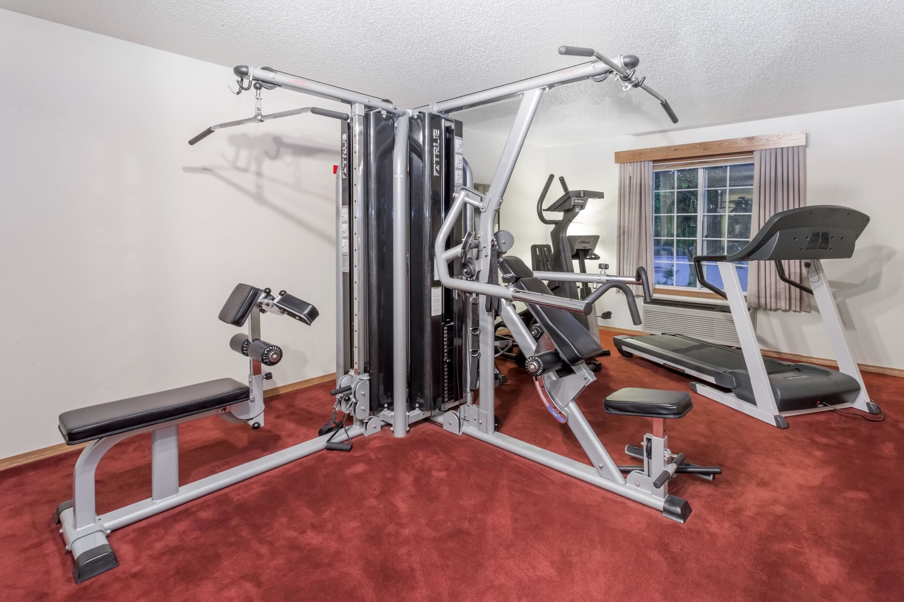 Une salle de sport à domicile équipée d’un appareil d’entraînement multifonctionnel, d’un tapis de course et d’un banc.