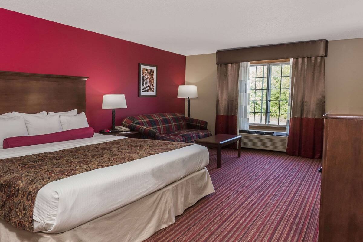 Ein Hotelzimmer mit einem großen Bett, einer Couch, einem Schreibtisch und einem Fenster mit Vorhängen.