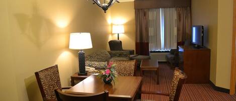 A hotel room with a dining area, a sofa, a TV, and a lamp.