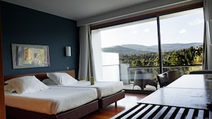 A modern hotel room with a large balcony, a bed, a desk, and a chair.