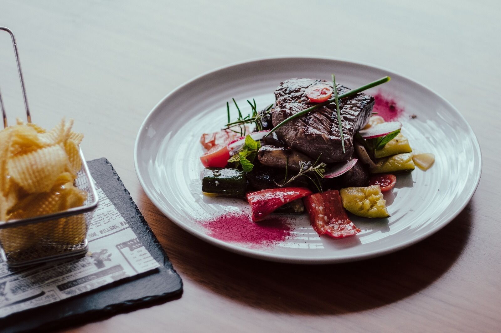 A plate of food with a steak, vegetables, and a small bowl of pasta.