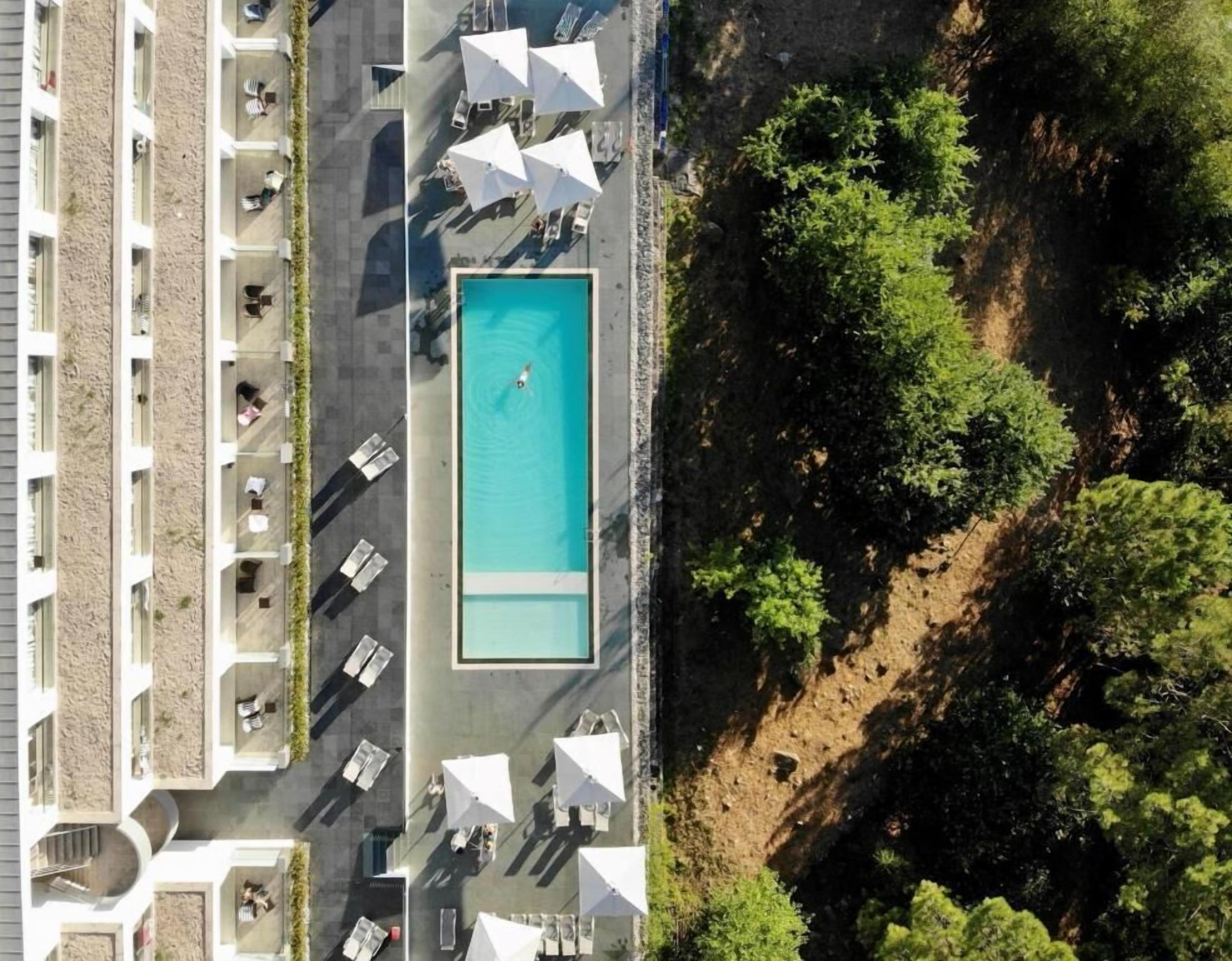 Vue aérienne d’un hôtel doté d’une piscine, d’un espace extérieur aménagé avec des sièges et d’un jardin avec des arbres.