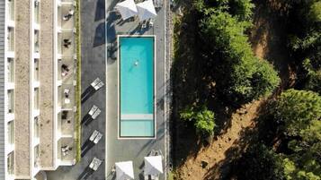 Vue aérienne d’un hôtel doté d’une piscine, d’un espace extérieur aménagé avec des sièges et d’un jardin avec des arbres.