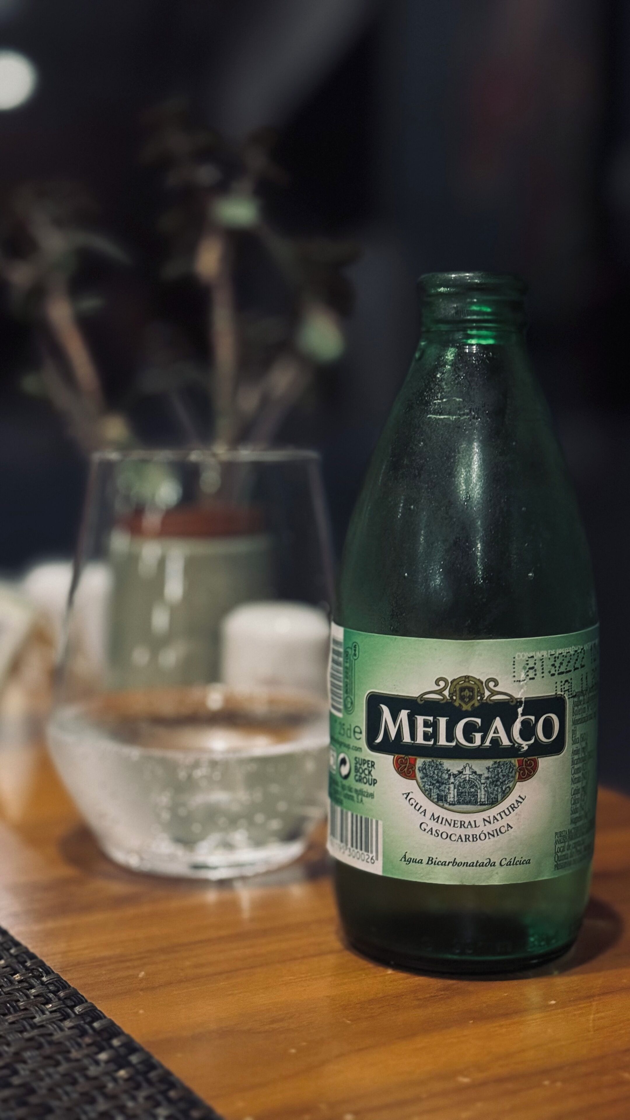 Una botella de cerveza Melgaço junto a un vaso sobre una mesa de madera.