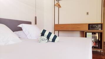 A neatly made bed with white and striped pillows, a wooden bedside table with a radio, and a wardrobe with a hanging rack.