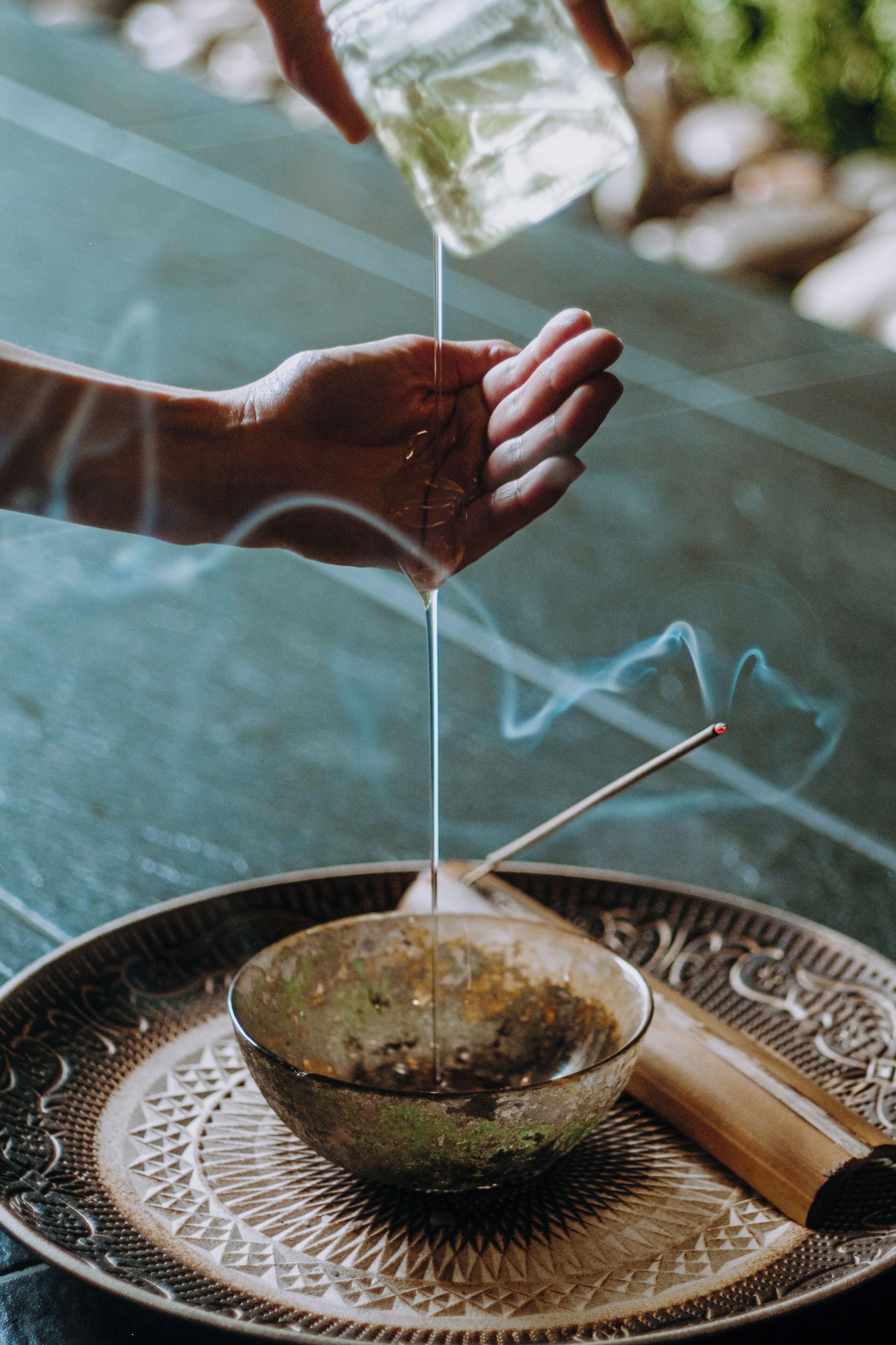A hand pouring liquid into a bowl with incense sticks.