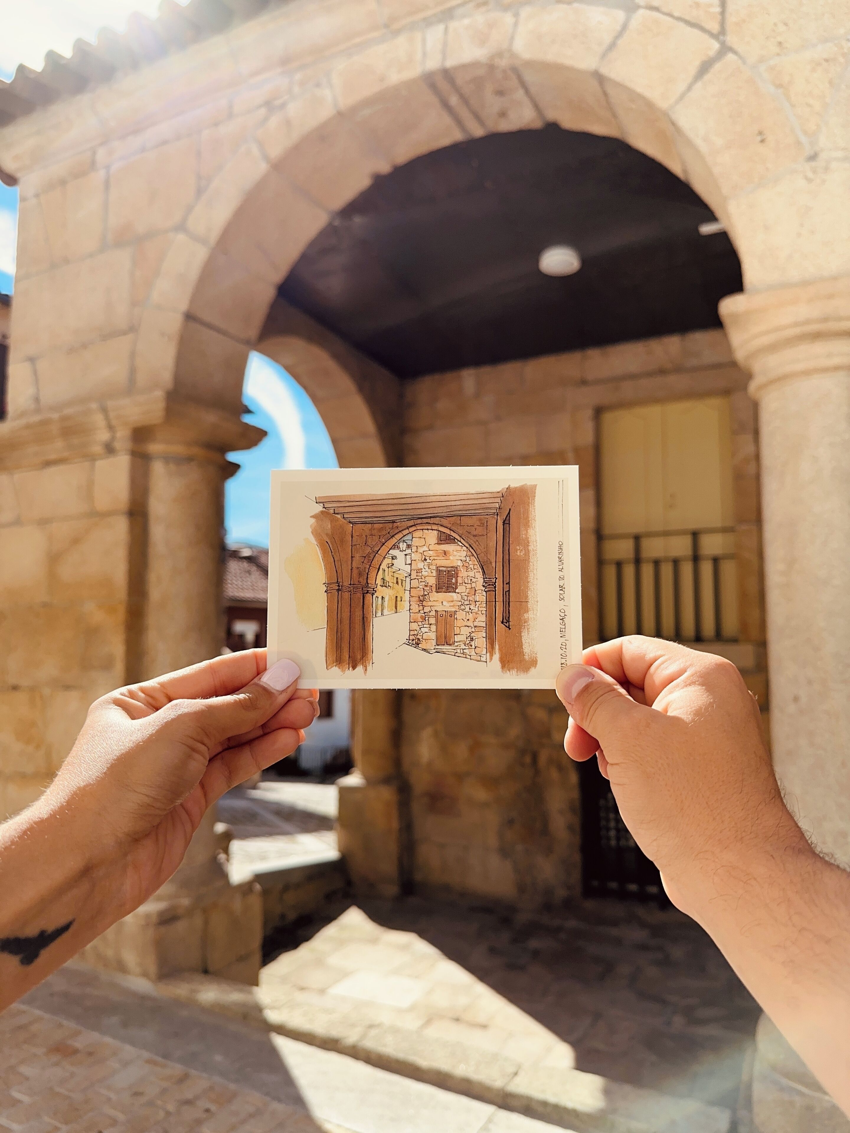A person holding a postcard with a drawing of a stone building with arches.