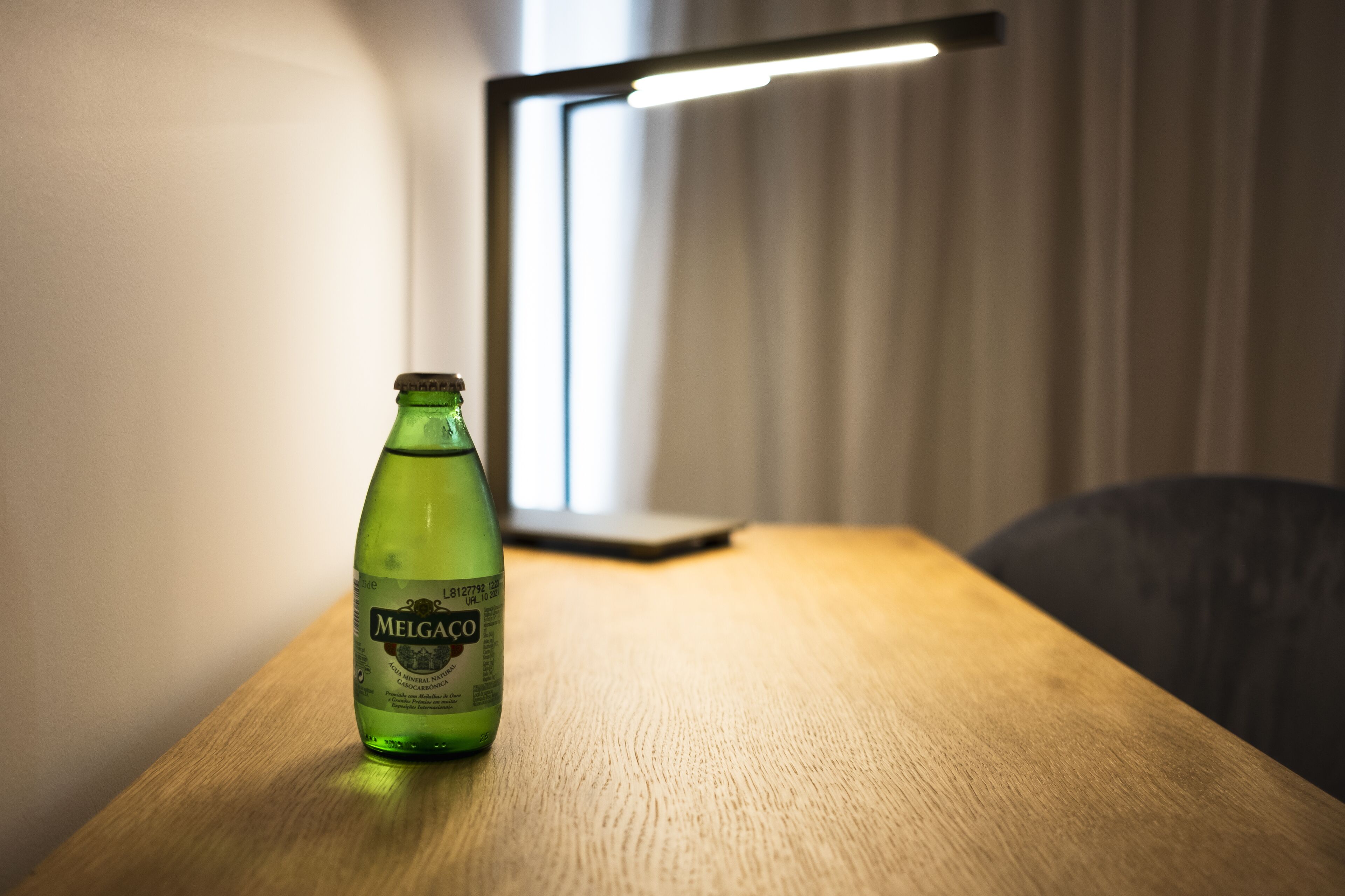 A bottle of Melgaço on a wooden table in a room with a window and blinds.