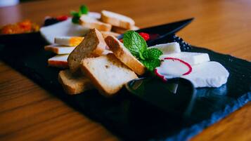 A black slate serving board with slices of bread, cheese, radishes, and mint leaves.
