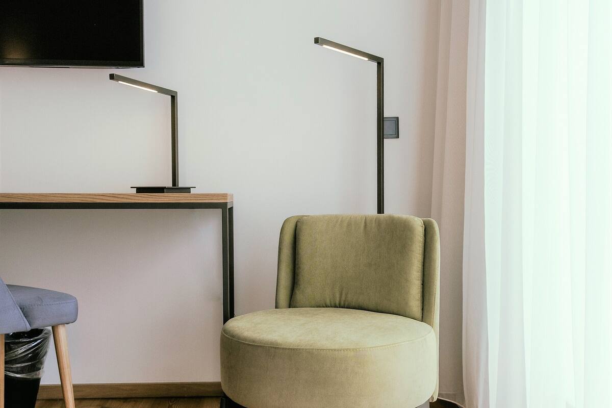 Una habitación de hotel moderna con suelo de madera, un sillón verde, un escritorio con televisor de pantalla plana y una cama.