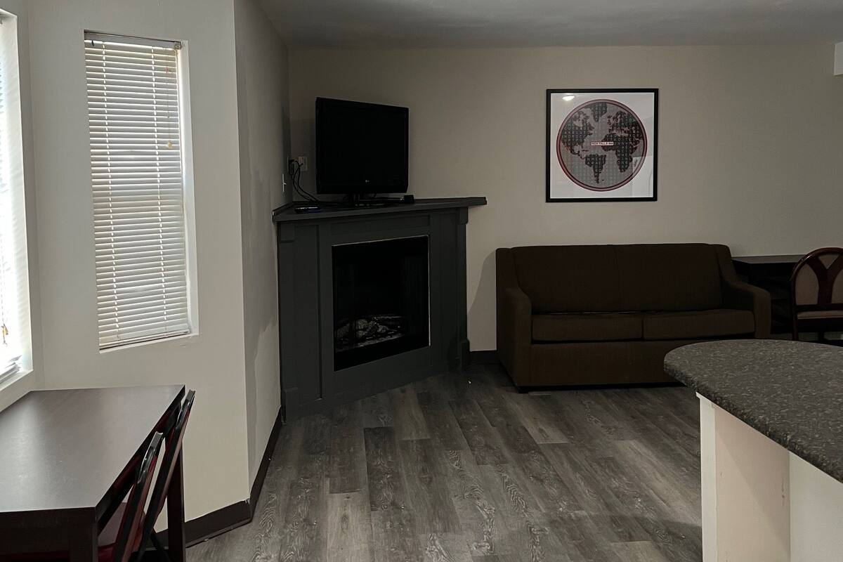 A living room with a fireplace, a television, a brown sofa, and a dining area with a table and chairs.