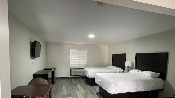 Habitación de hotel con dos camas, un escritorio, una silla, un televisor y una ventana con persianas.