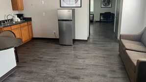 Una cocina moderna con refrigerador, armarios de madera y un comedor con sofá y mesa.