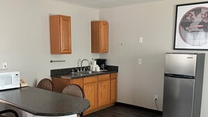 Una cocina moderna con armarios de madera, encimera de granito y electrodomésticos de acero inoxidable, incluyendo un refrigerador y un microondas.