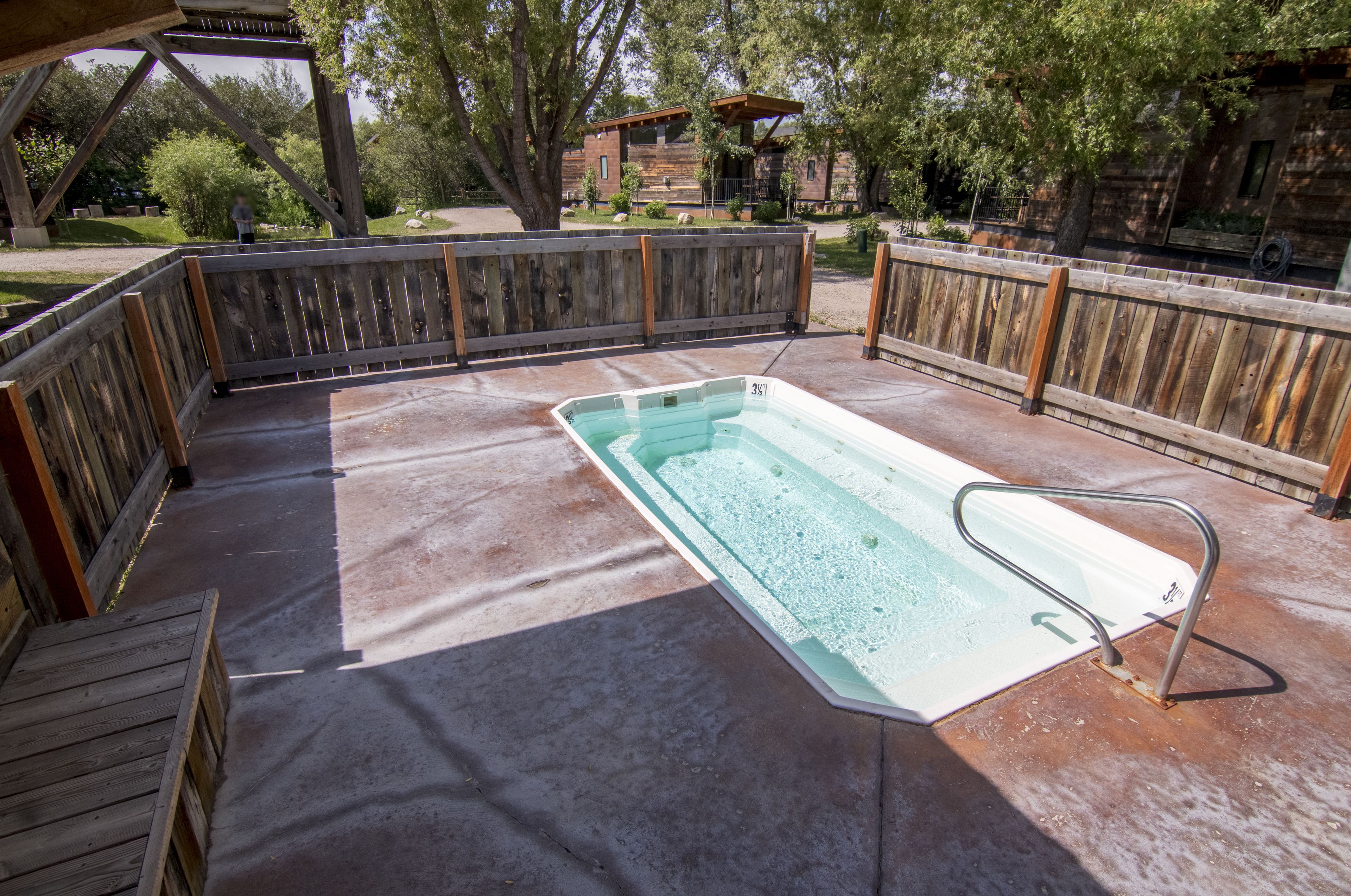 A rectangular swimming pool with a metal ladder, surrounded by a wooden deck and a wooden fence.