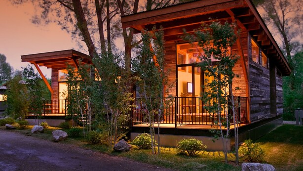 A modern log cabin with a large porch and a covered outdoor seating area.