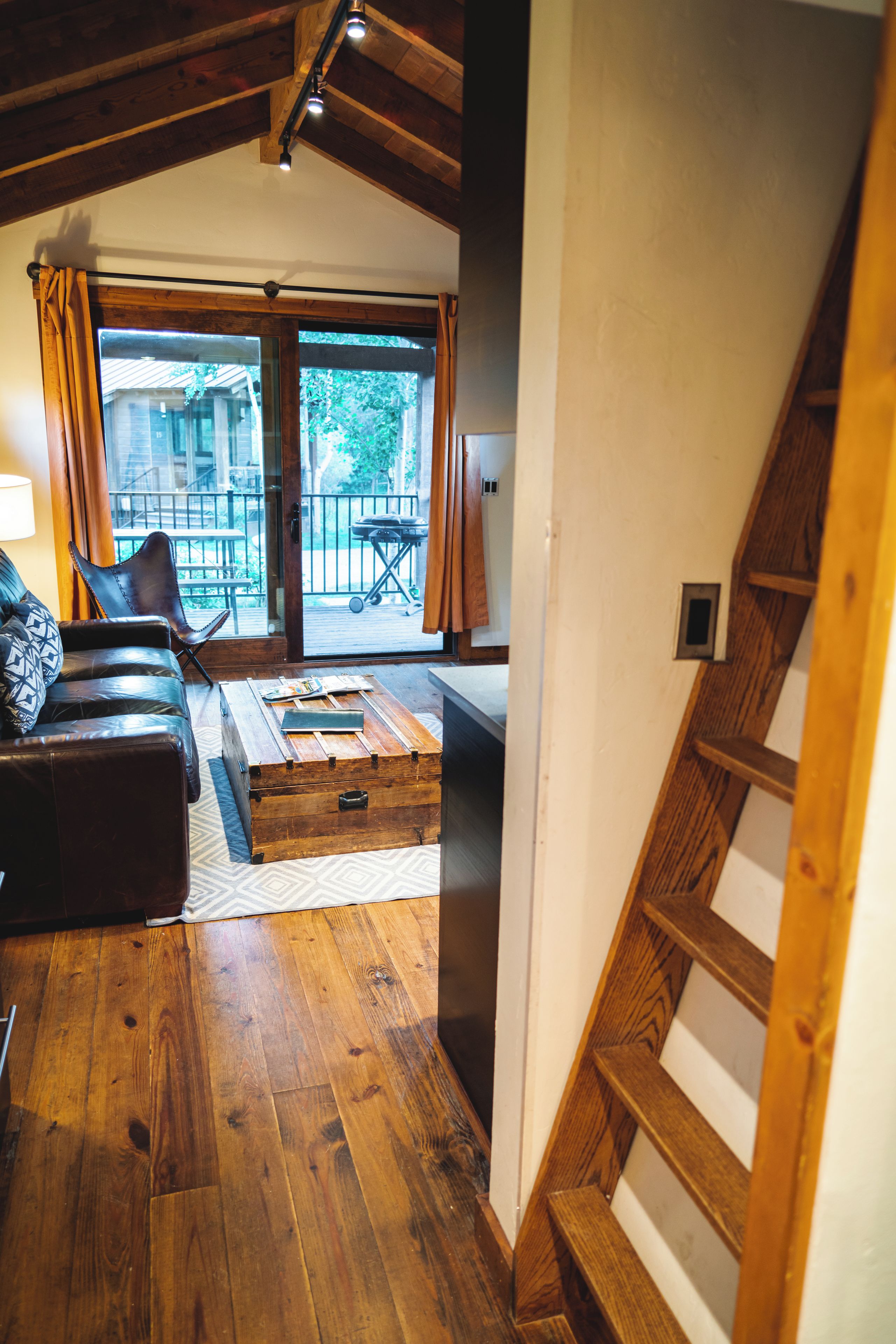 Un salon au plancher de bois, avec un canapé, une table basse et une vue sur un balcon aménagé avec du mobilier d’extérieur.
