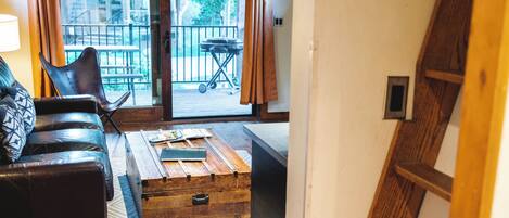 Un salon au plancher de bois, avec un canapé, une table basse et une vue sur un balcon aménagé avec du mobilier d’extérieur.