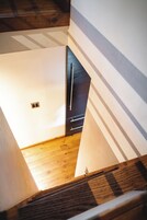 Una escalera baja a un nivel inferior con piso de madera y una puerta oscura.