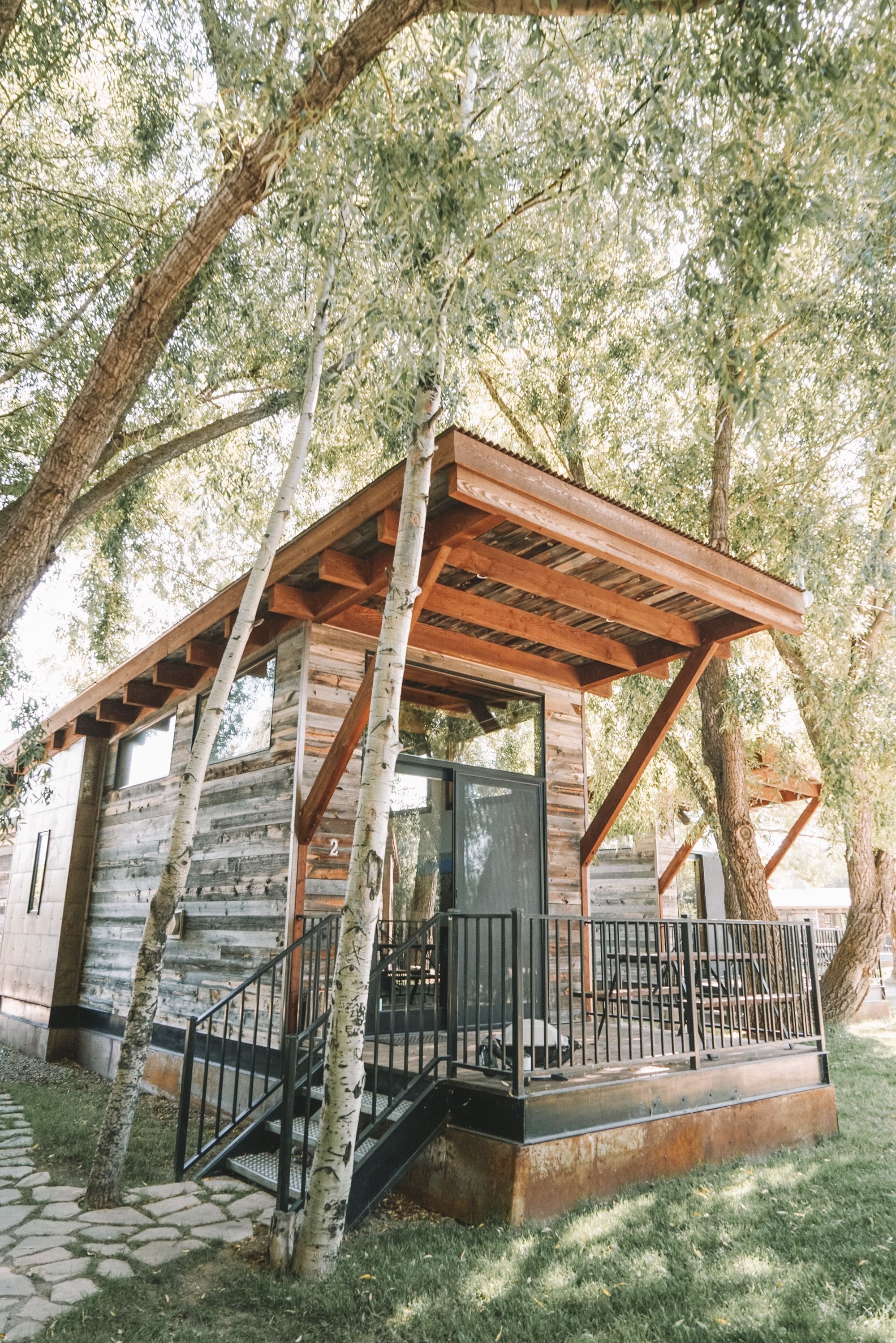 A rustic cabin with a wooden porch, stone steps, and a metal railing.