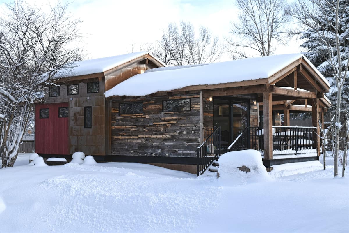 A rustic cabin with a stone exterior, wooden porch, and a red door.