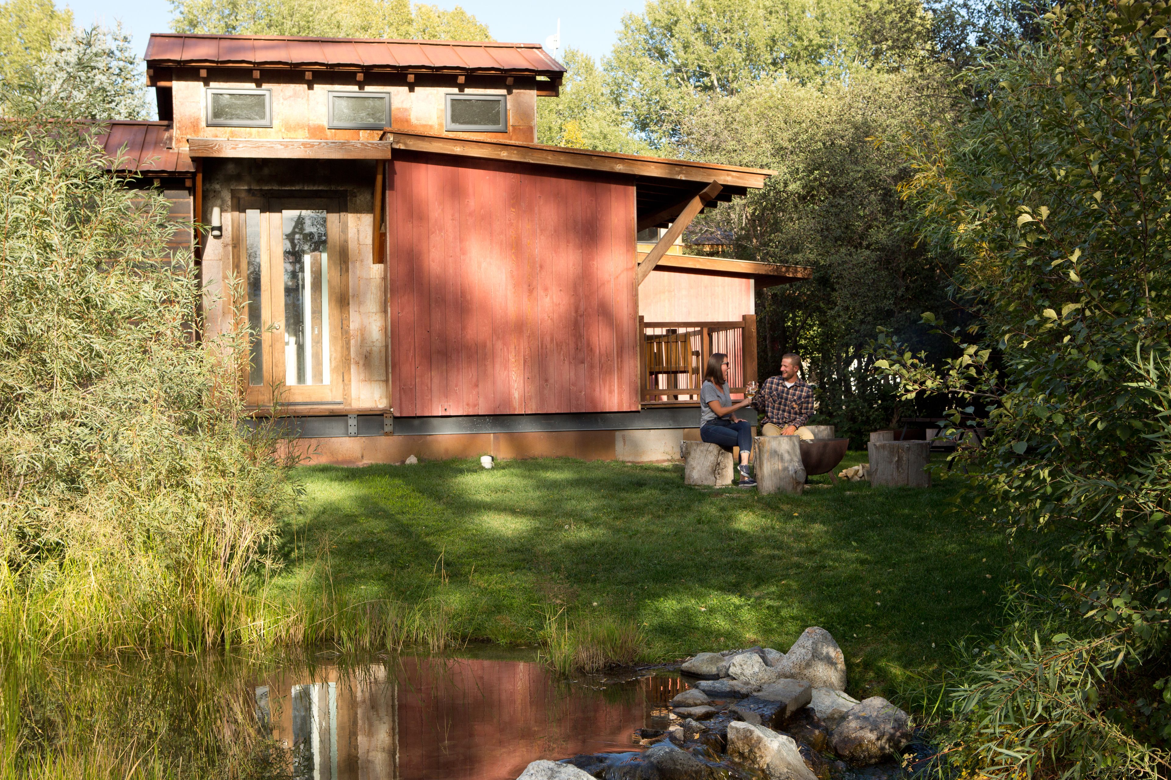 A rustic wooden building with a pond in front, surrounded by greenery.
