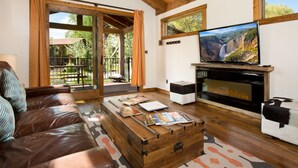 A living room with a leather sofa, a wooden coffee table with magazines, a fireplace, and a TV on a wooden stand.