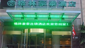L’entrée d’un hôtel, avec une enseigne illuminée en vert au-dessus des portes et un message de bienvenue en chinois.