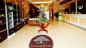 A hotel lobby with a reception desk, a floral centerpiece, and a 'Green Tree' sign on the floor. - GreenTree Inn Guangzhou Panyu Bus Station Business Hotel (Guangzhou)
