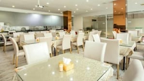 A modern dining area with glass tables and white chairs, a kitchen in the background, and a ceiling with recessed lighting. - GreenTree Inn Guangzhou Panyu Bus Station Business Hotel (Guangzhou)