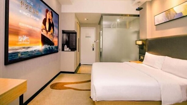 A hotel room with a large bed, a flat-screen TV mounted on the wall, a small table, and a glass door leading to a bathroom. - GreenTree Inn Guangzhou Panyu Bus Station Business Hotel (Guangzhou)