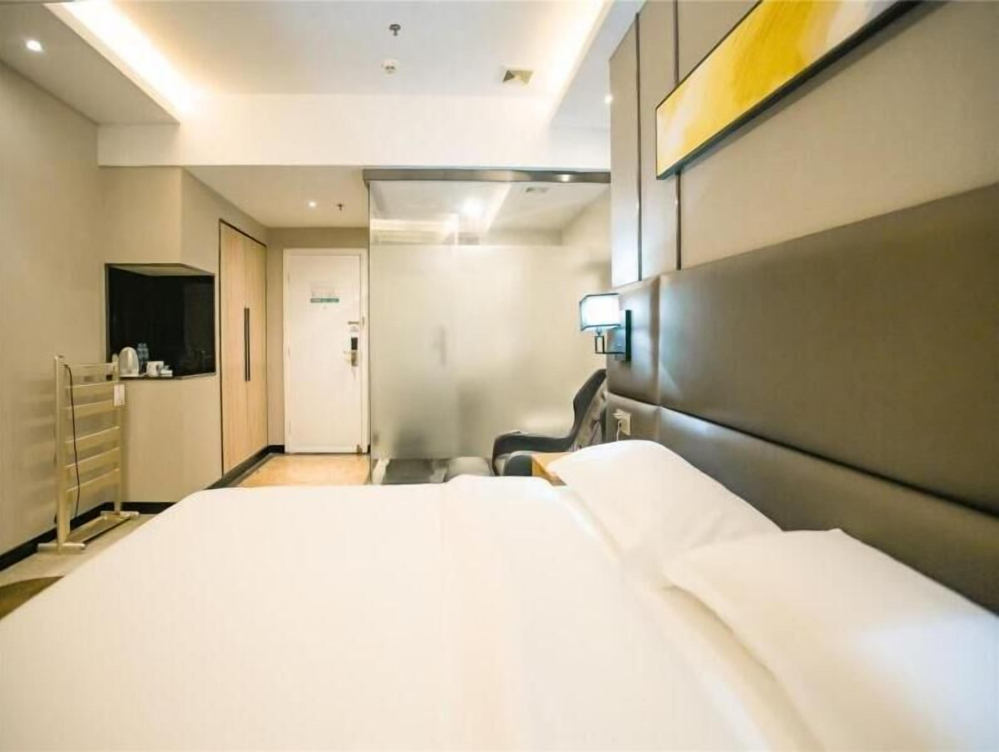 A modern hotel room with a large bed, a bedside table, a chair, a mirror, and a door leading to a bathroom.