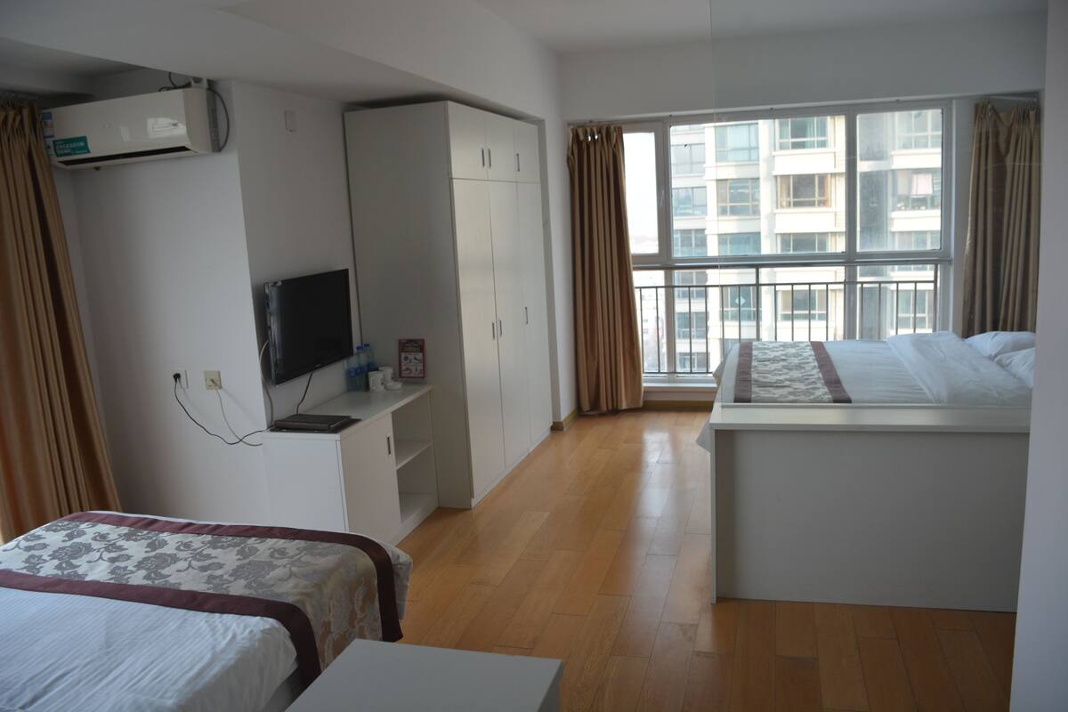 A hotel room with a bed, a desk, a wardrobe, a TV, and a window with curtains.
