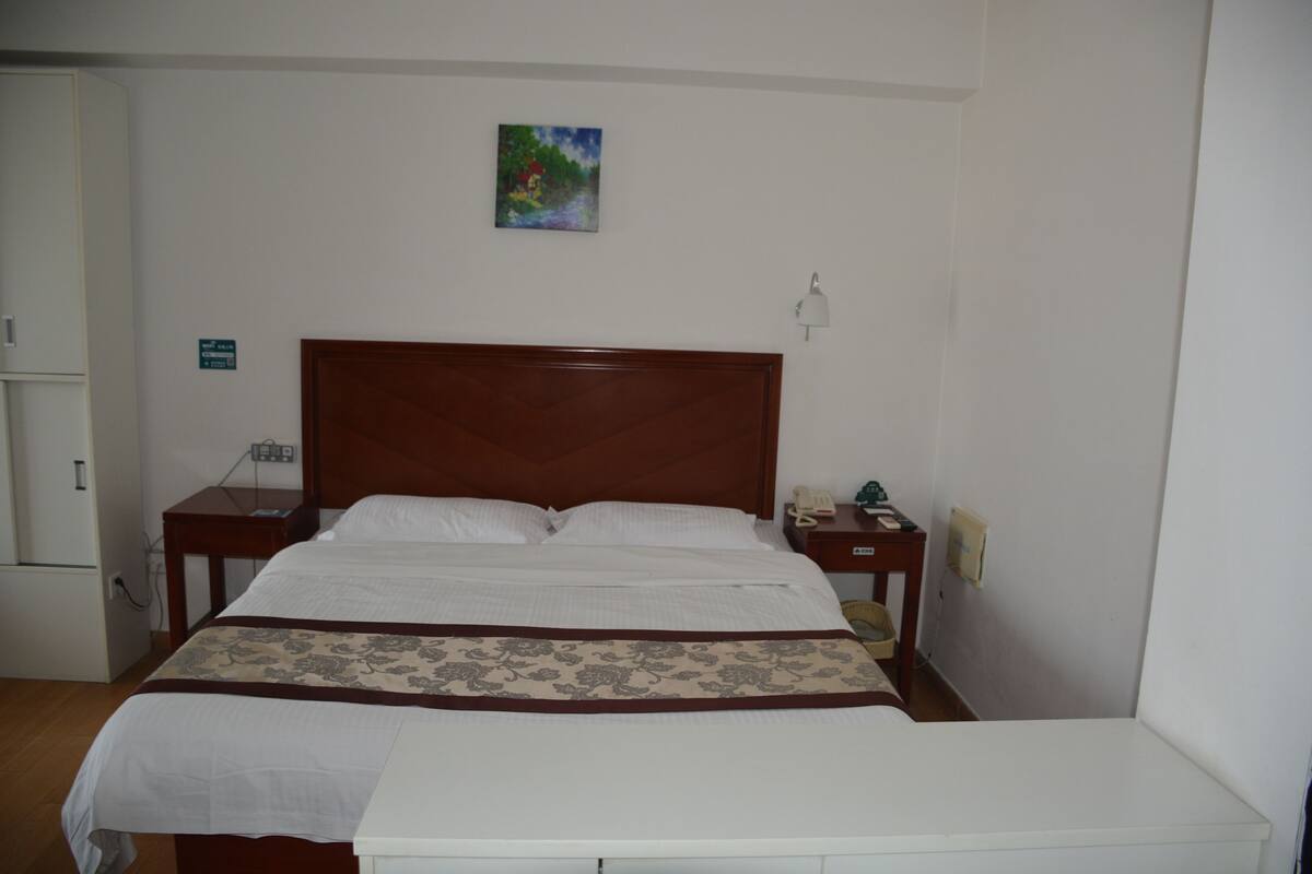 A neatly made bed with a wooden headboard, a bedside table with a lamp, and a small painting on the wall.