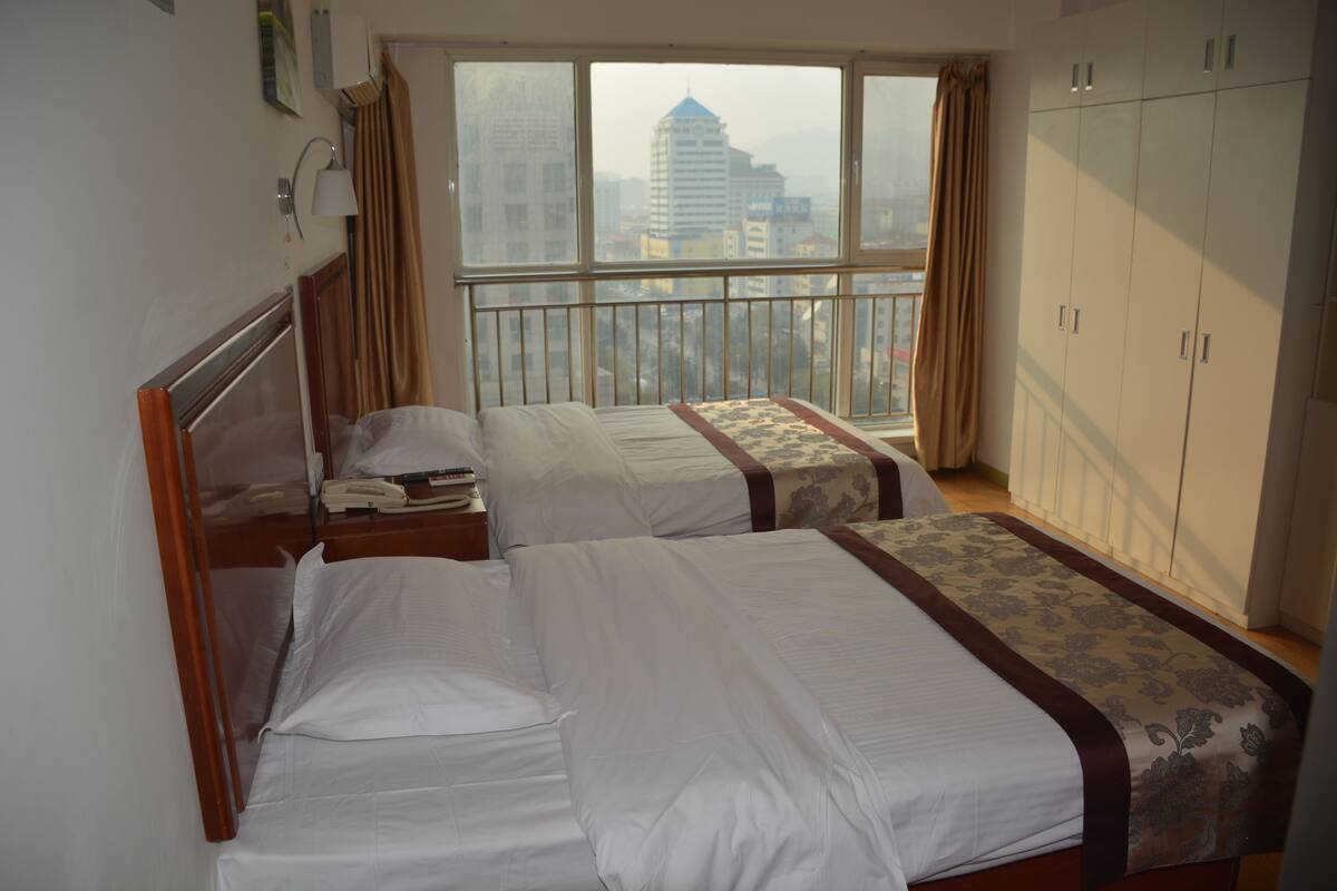 A hotel room with two beds, a wardrobe, and a balcony with a city view.