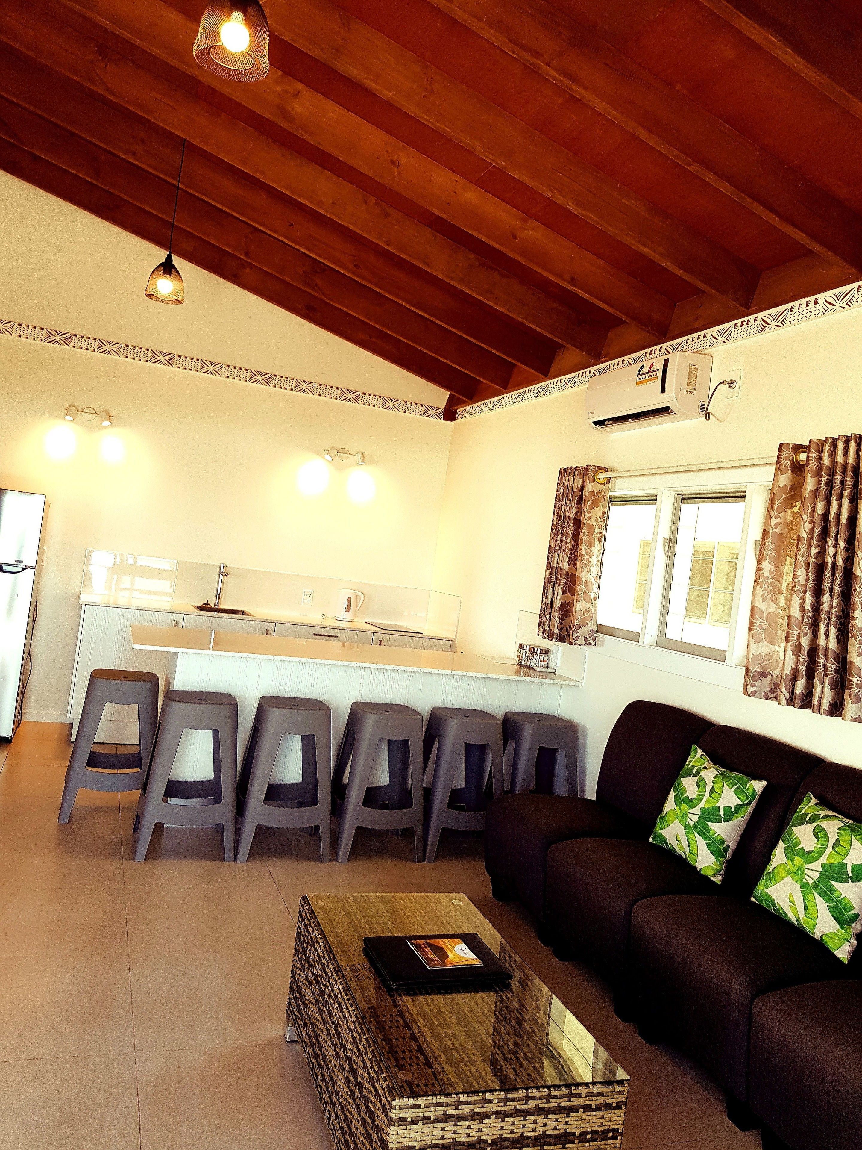 A living room with a sofa, a coffee table, and a kitchen area with stools.