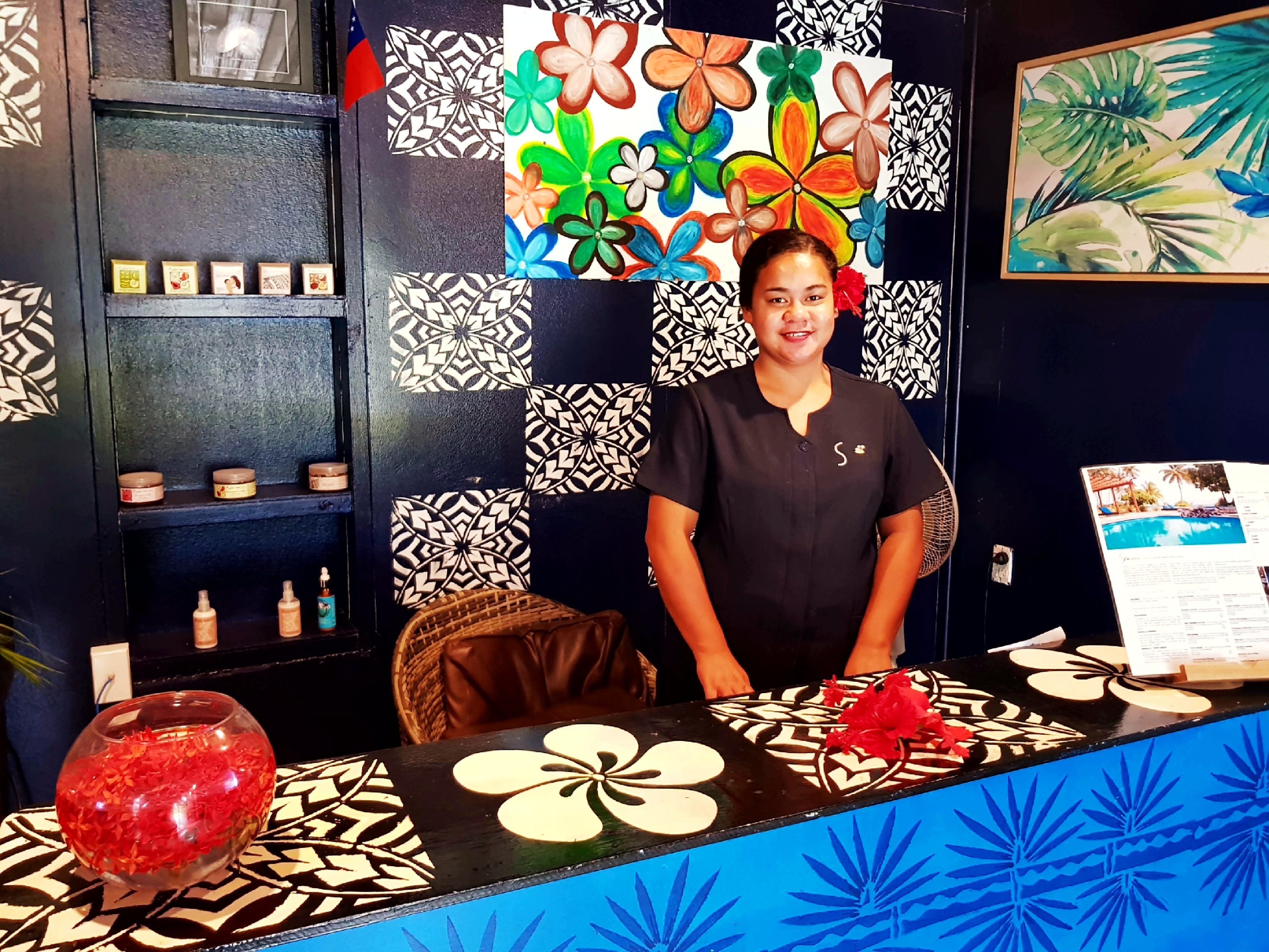 A reception area with a black and white patterned wall, a colorful flower painting, a small wicker chair, and a glass bowl with red flowers.