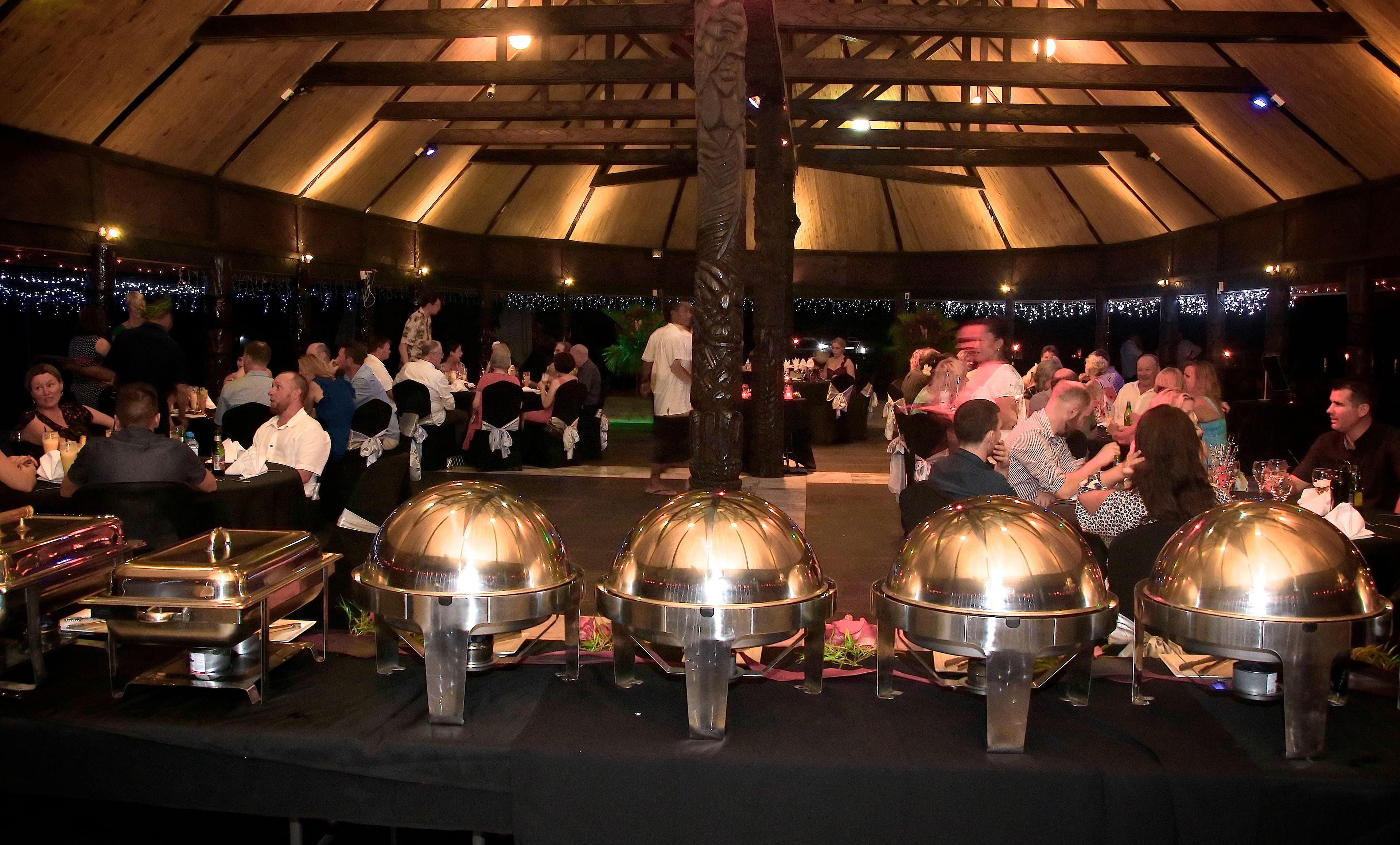 A covered outdoor dining area with round, metallic serving stations and a wooden ceiling structure.