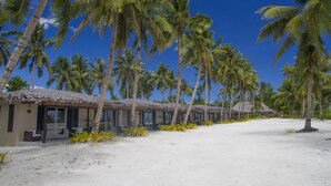 Un hotel frente a la playa con edificios de techo de paja, palmeras y una playa arenosa.