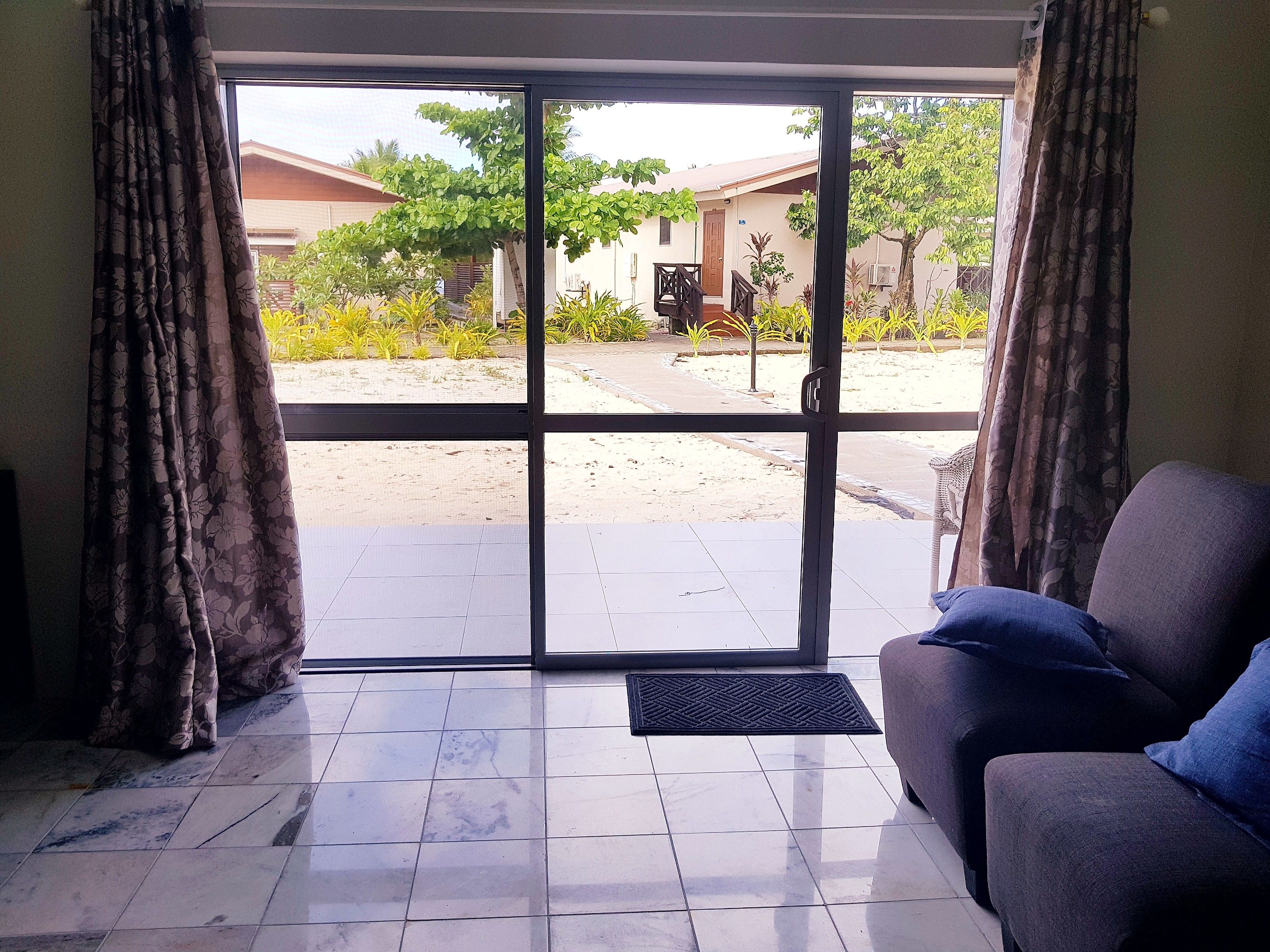 A room with a sliding glass door leading to a covered outdoor area, a sofa, and a tiled floor.